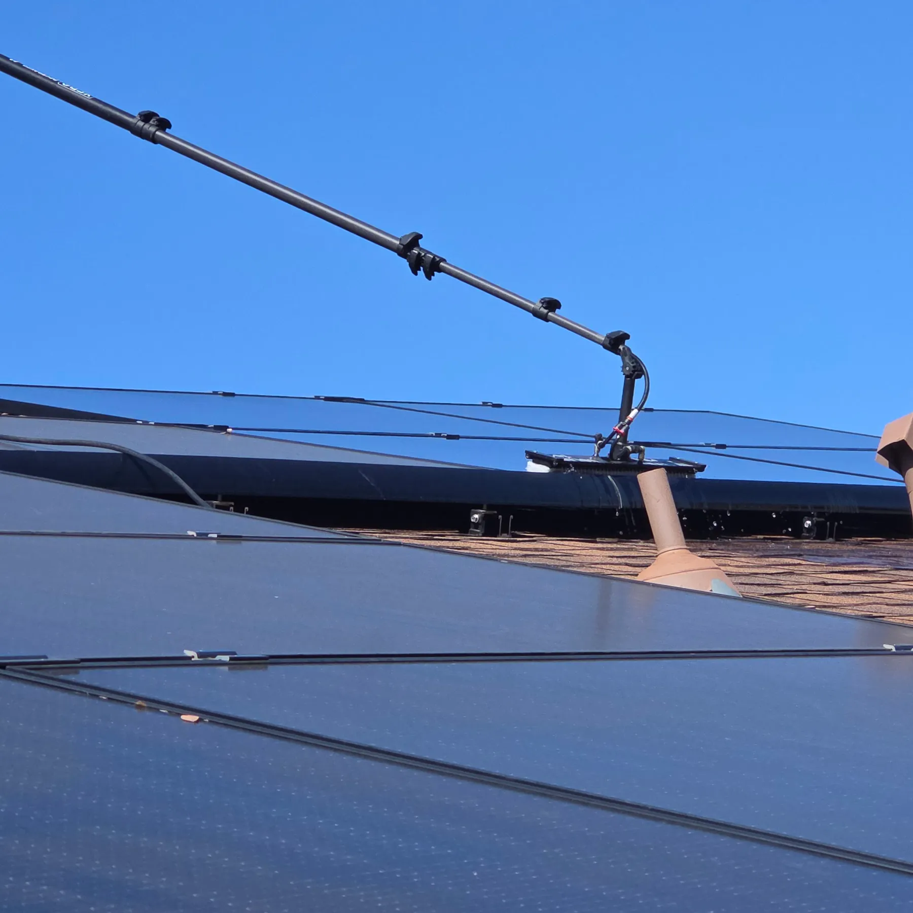 A water-fed cleaning pole resting across rooftop solar panels during a cleaning visit